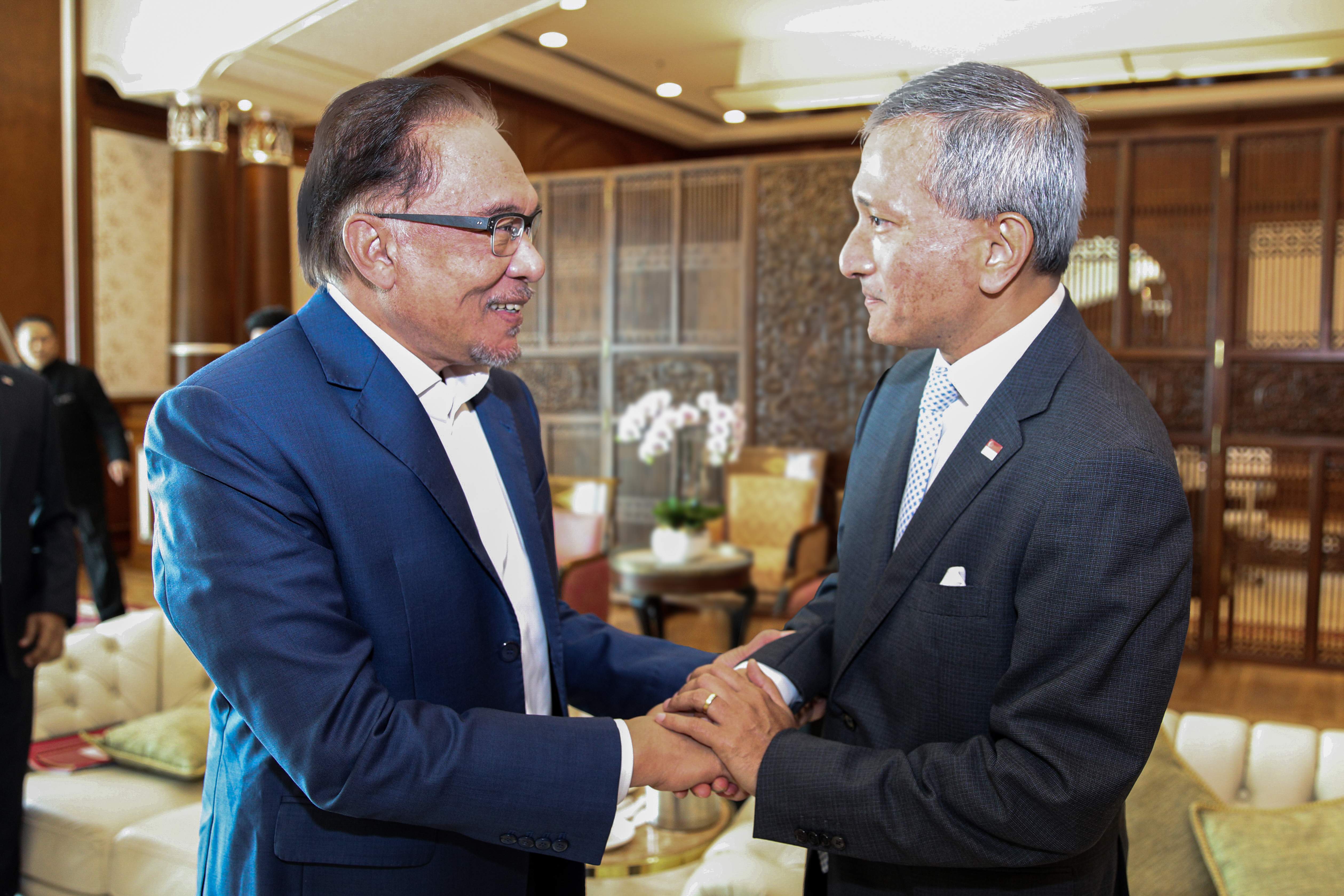 Anwar Ibrahim, in a blue suit, shakes hands with a man in a gray suit indoors.